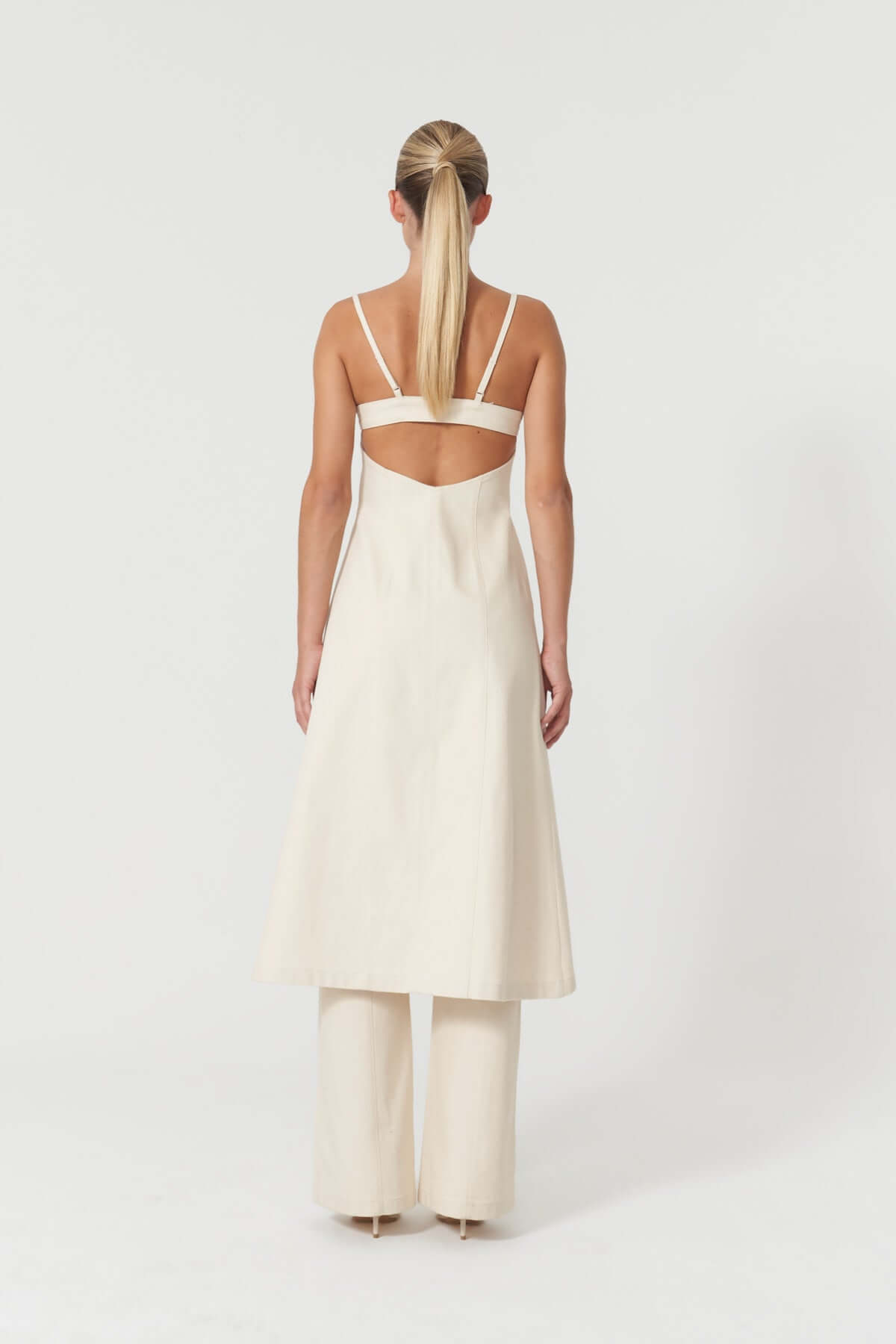 Stylish beige midi dress by JENDUE Davidson, highlighting its contemporary cut with a visible silver zipper and a long, dramatic slit.