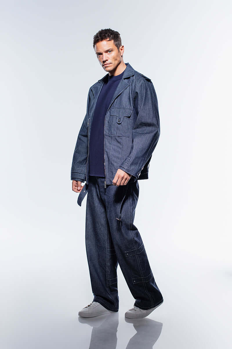 A classic yet modern men's navy blue denim jacket, with a front zipper and a stylish belted hem, highlighted by white stitching.