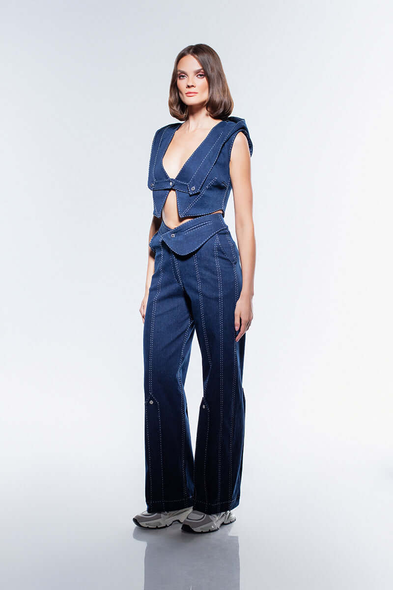 A pair of navy blue, high-waisted, straight-leg jeans. The design is detailed with white contrast stitching and silver buttons on the hem.