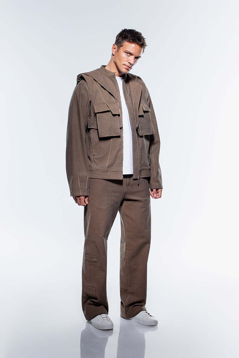A men's brown denim jacket with a high collar, detachable hood, and prominent white stitching on the seams and large chest pockets.